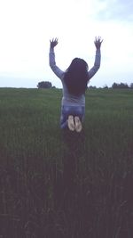 Woman jumping over field against sky