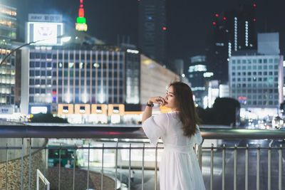 Woman standing by railing in city at night