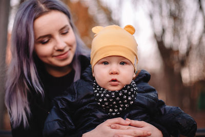 Happy young mother holding baby son while sitting on bench in park