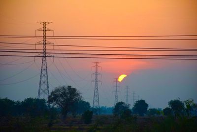 Low angle view of electricity pylon against sky during sunset