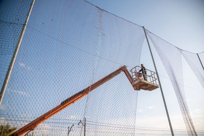 Low angle view of man working while standing on crane