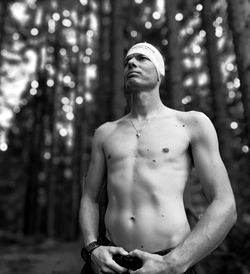 Full length of shirtless man standing against tree