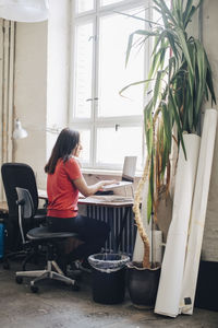 Side view of businesswoman using laptop at desk in creative office