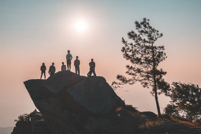 Low angle view of friends standing on rock formation against clear sky during sunset