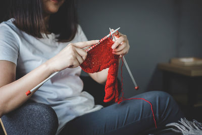 Midsection of young woman knitting wool while sitting on armchair at home
