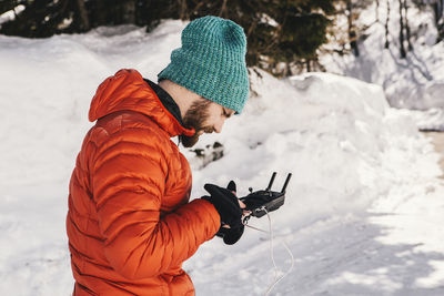 Side view of man using remote control while standing on snow covered field