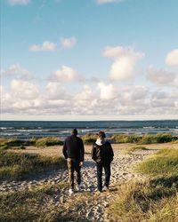 Rear view of two people walking on beach