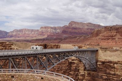 Vehicles on bridge over rock formation at grand canyon national park against sky