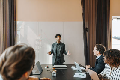 Young male entrepreneur explaining strategies to colleagues sitting in board room at office