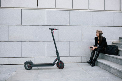 Side view of woman sitting on bicycle against wall