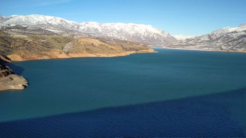 Scenic view of sea and snowcapped mountains against blue sky