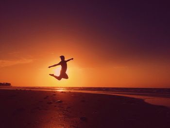 Silhouette of woman jumping on beach at sunset