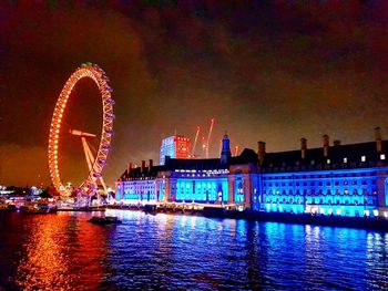 Illuminated ferris wheel in city against sky at night