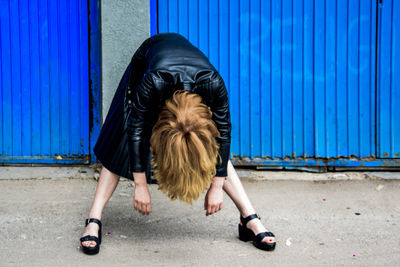 Woman bending over against blue corrugated iron wall