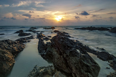 High angle view of rock formations in sea against cloudy sky at sunset