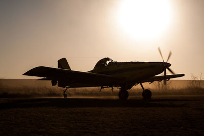 Silhouette airplane on field against sky during sunset