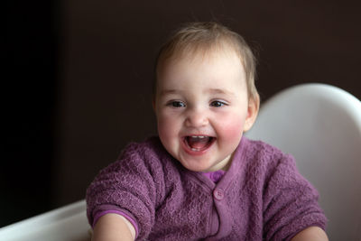 Cute carefree laughing baby sitting on baby chair. baby is wearing lilac knitted overall. 