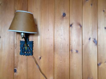 Close-up of electric lamp hanging against wooden wall