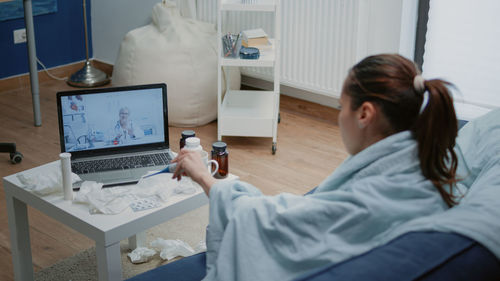 Rear view of woman using laptop at home