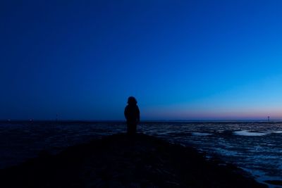 Silhouette man looking at sea against clear blue sky