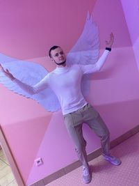 Full length portrait of young woman standing against pink wall