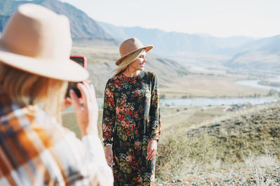 Two young stylish women travel in the mountains, shoot each other on smartphone