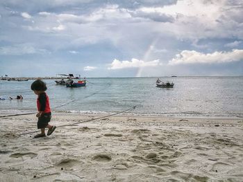 Rear view of boy standing on beach against sky