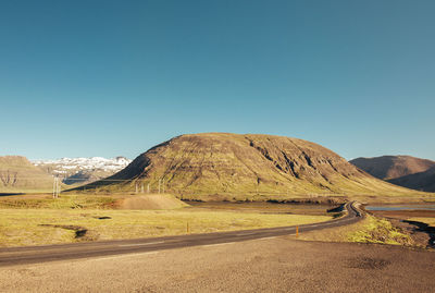 Scenic view of road by mountains against clear blue sky