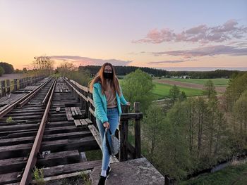 Woman standing on railroad track against sky during sunset