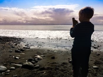 Rear view boy of standing on beach against sea