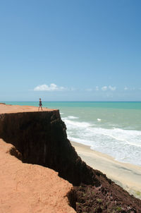 Woman standing on mountain by sea against blue sky