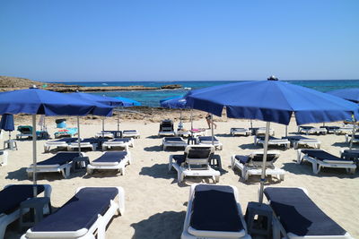Empty lounge chairs and parasols at beach against clear blue sky