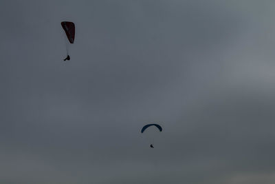 Low angle view of people paragliding against sky