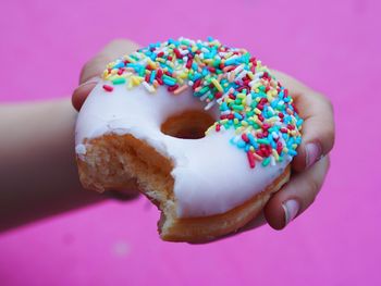 Cropped hand holding donut against pink wall