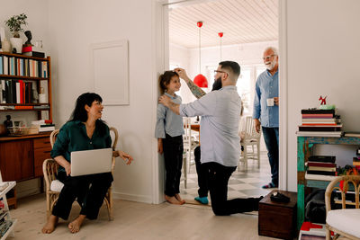 Happy family looking at man measuring daughter's height against wall at doorway