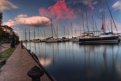 Sailboats moored on harbor against sky during sunset