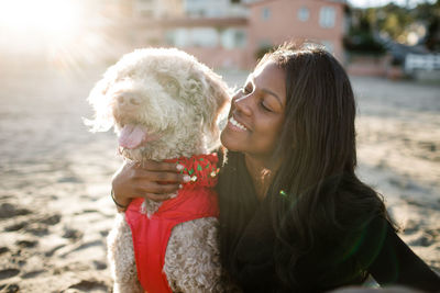 Young girl hugging labradoodle on beach at sunset