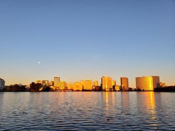 River by buildings in city against clear sky during sunset