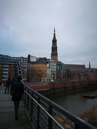 Rear view of people walking on bridge against buildings in city