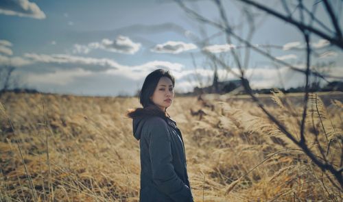 Portrait of young woman standing on field against sky