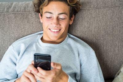 High angle view of smiling teenage boy using mobile phone on sofa