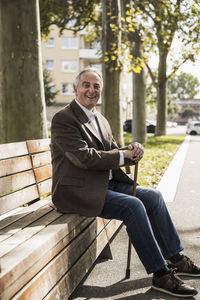 Happy senior man with walking cane sitting on bench