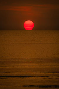 Red balloon on sea against sky during sunset