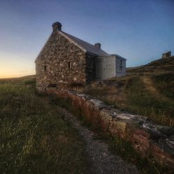 Old house on grassy field against sky