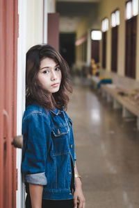 Portrait of confident young woman leaning on wall while standing in corridor