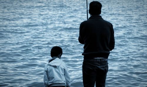 Rear view of father with son standing in sea