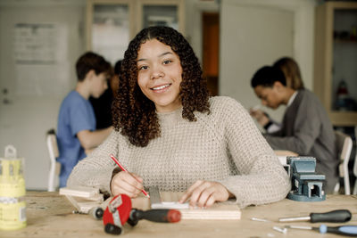 Portrait of smiling female teenage student during carpentry class at high school