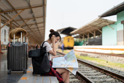 Side view of young woman sitting on railroad station