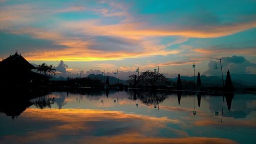 Silhouette buildings by lake against sky during sunset