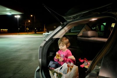 Girl eating food while sitting in car trunk
